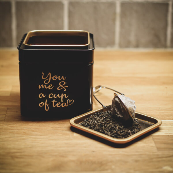 Graverad teburk i svart och guld. Text: You me & a cup of tea